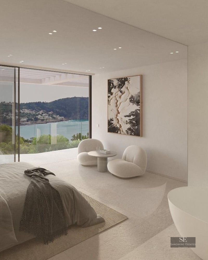 Modern bedroom with floor-to-ceiling windows overlooking a bay, featuring a freestanding tub and designer furniture.