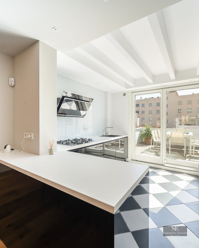 Modern kitchen featuring a black and white checkered floor, white ceiling beams, and large glass doors to a sunny terrace.