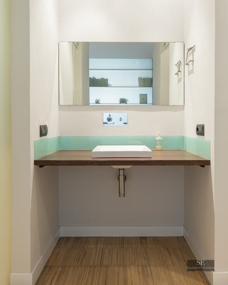 Bathroom featuring a floating wood countertop, white square vessel sink, rectangular mirror, and teal glass backsplash.