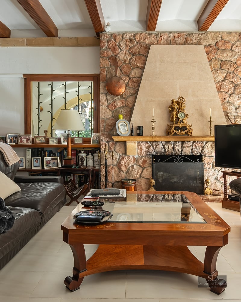 A cozy living room featuring dark leather sofas, a large stone fireplace, and exposed wooden ceiling beams.
