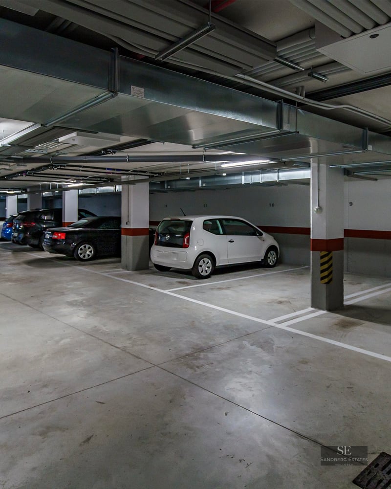 Well-lit underground parking garage with numbered stalls, parked cars, and overhead ventilation ducts.