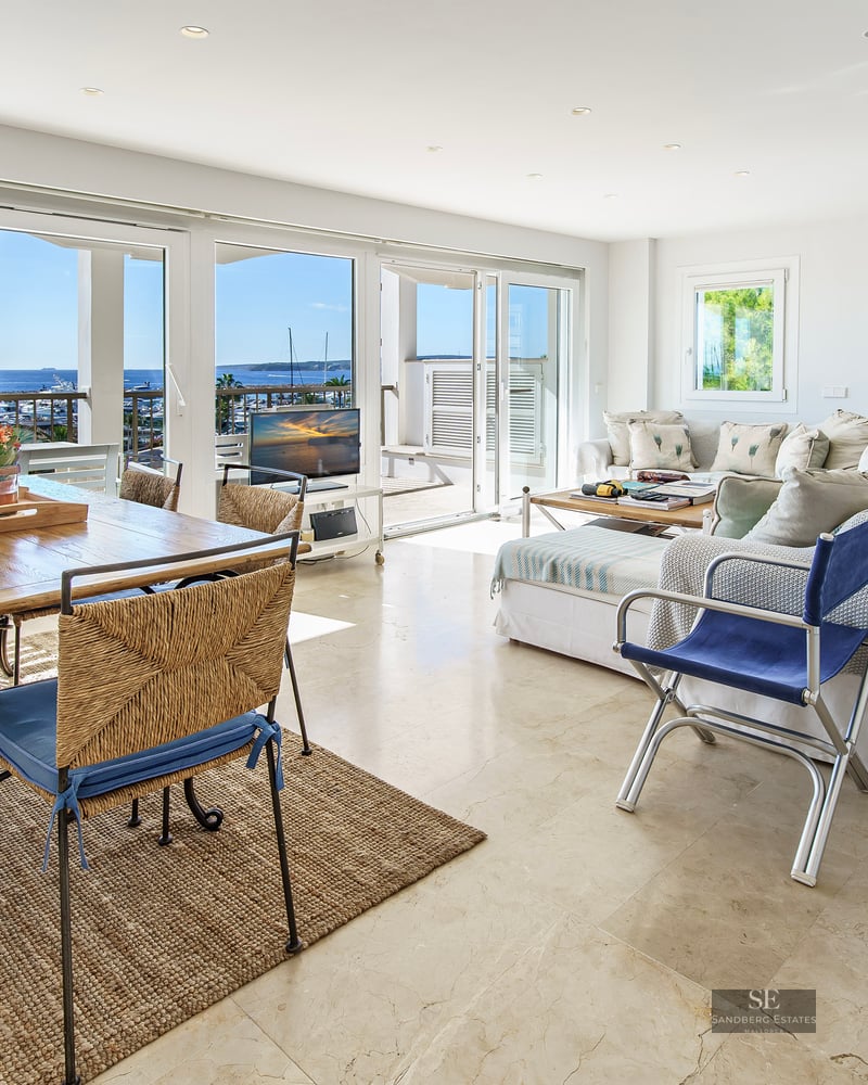 Open-plan living room with marble floors and large windows overlooking a marina and sea.