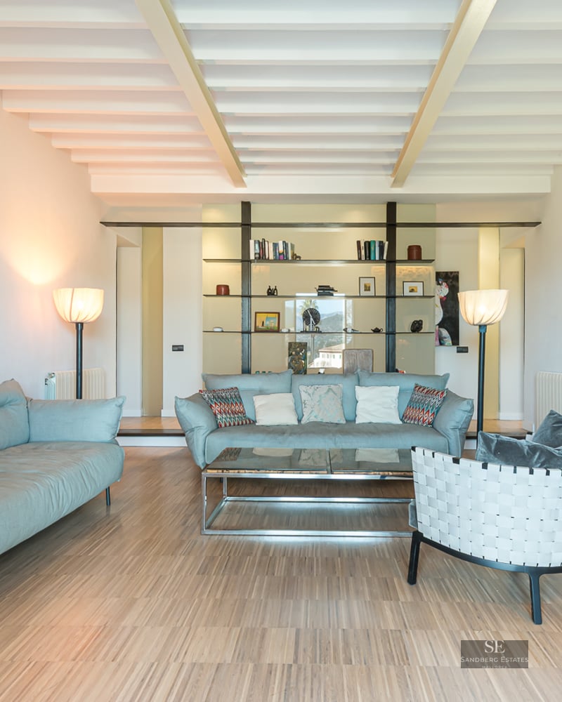 Spacious living room with light blue sofas, white beamed ceiling, wooden floors, and large abstract paintings.