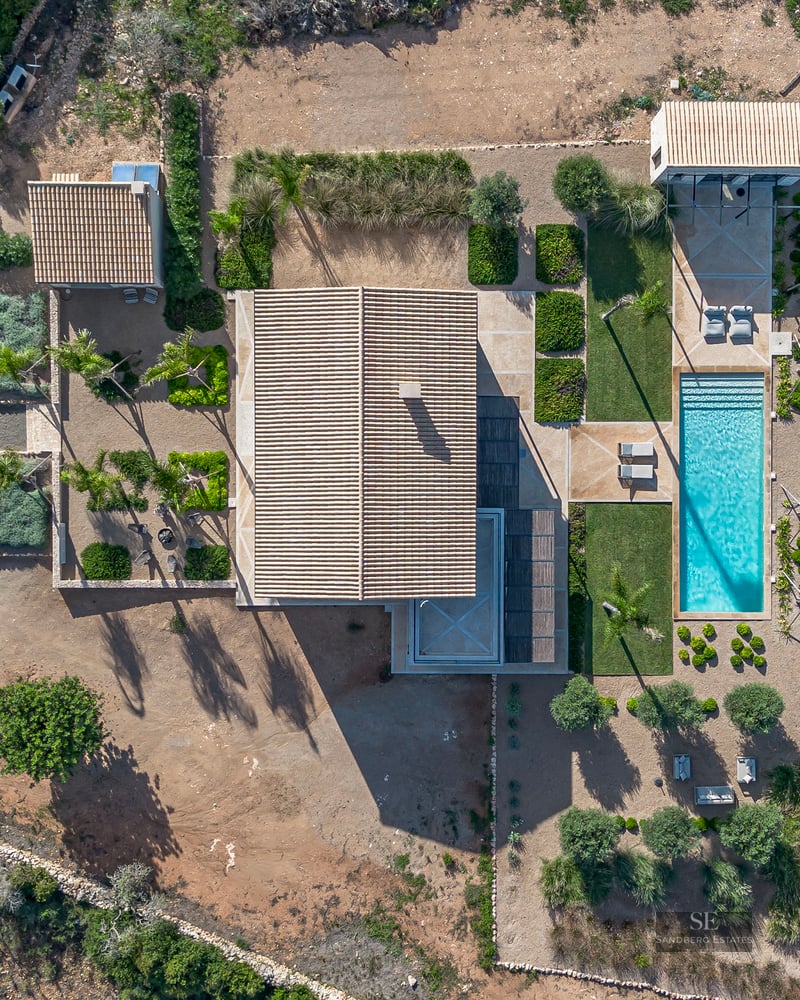 Bird's eye view of a modern villa with a turquoise pool, landscaped gardens, and terracotta roofs.