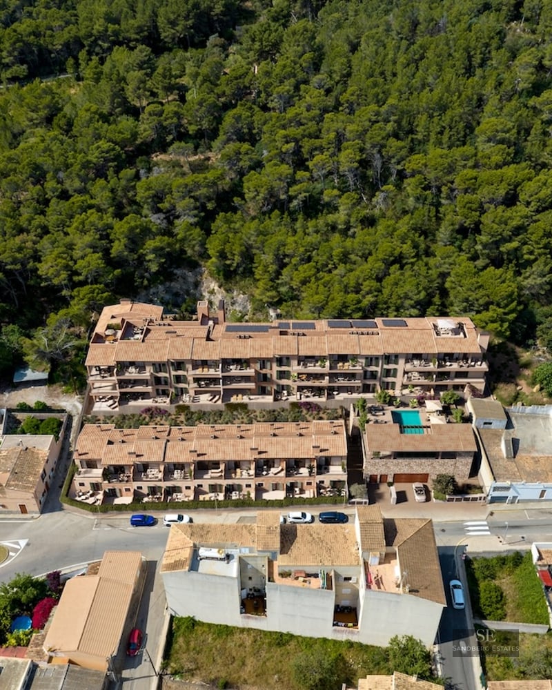 Drone shot of a Mediterranean-style apartment complex with terracotta roofs nestled against a dense green forest.