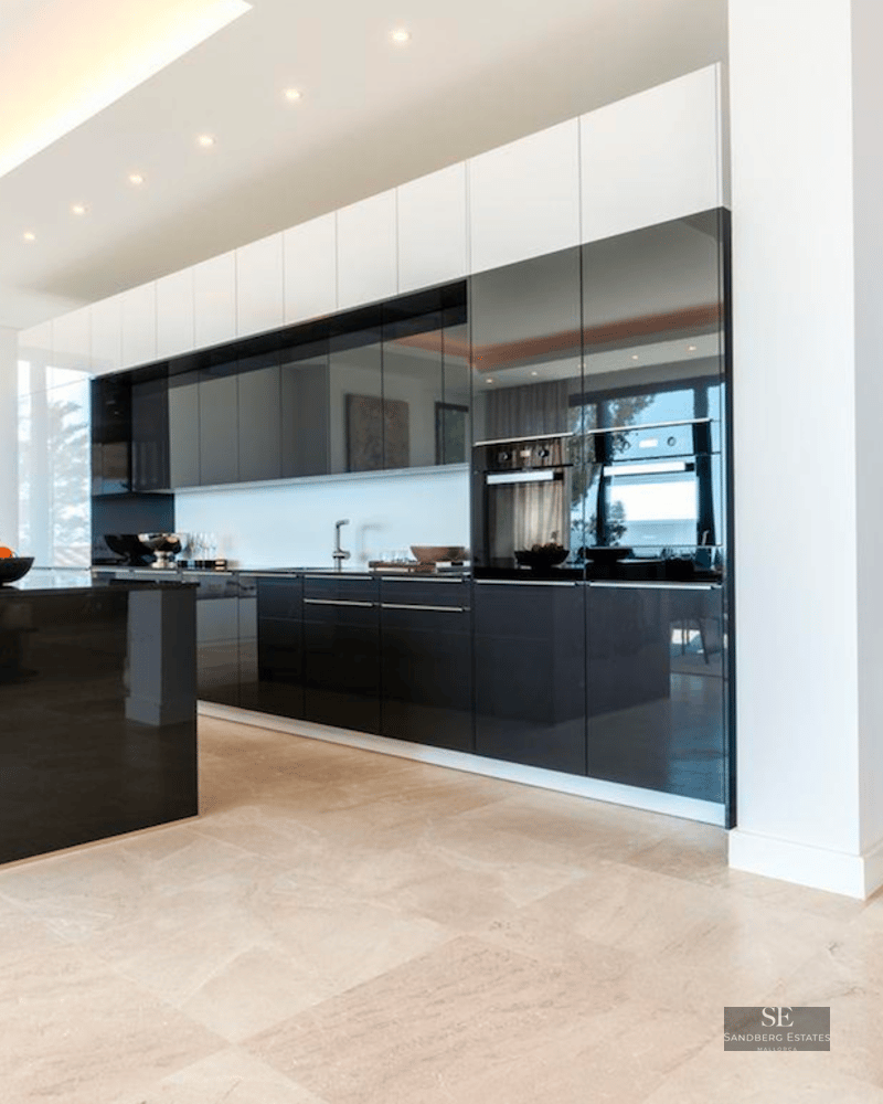 Spacious modern kitchen featuring a large black glossy island, dark cabinetry, and light stone flooring.