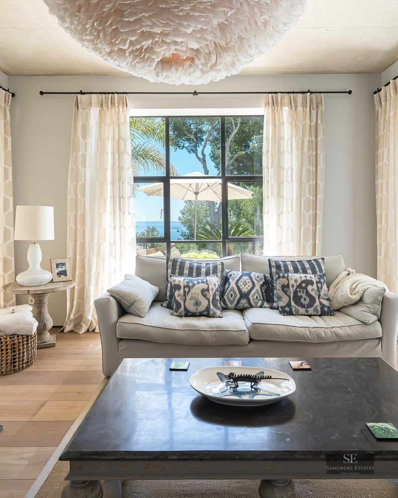 Bright living room with a stone fireplace, plush sofa, and large glass doors opening to a turquoise swimming pool.