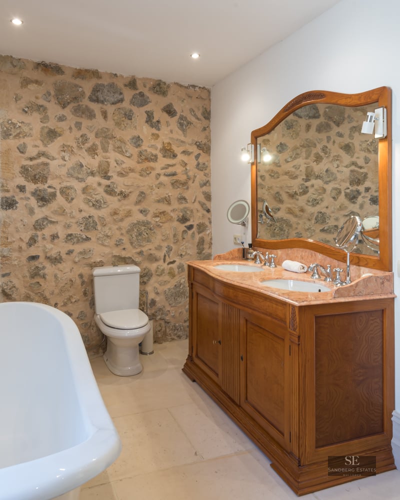 Elegant bathroom with a rustic stone wall, double wooden vanity, freestanding tub, and glass shower enclosure.