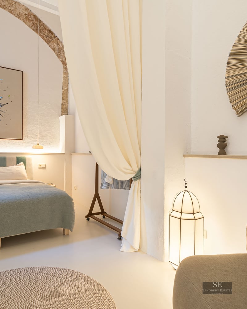 Chambre de luxe avec grand lit, arche en pierre d'origine, rideaux fluides et décor méditerranéen minimaliste.