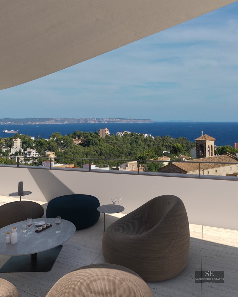 Modern rooftop terrace with designer lounge seating overlooking a Mediterranean coastal city and the blue sea.