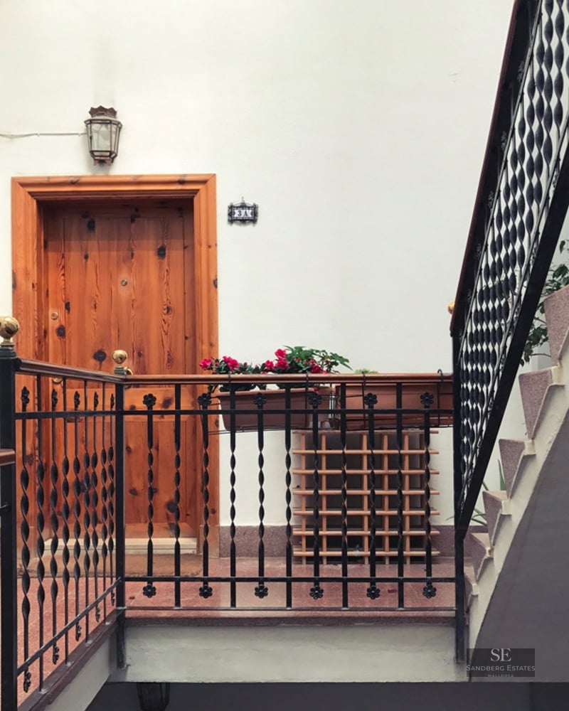 Bright building landing featuring solid wood doors, wrought iron railings, and white walls.