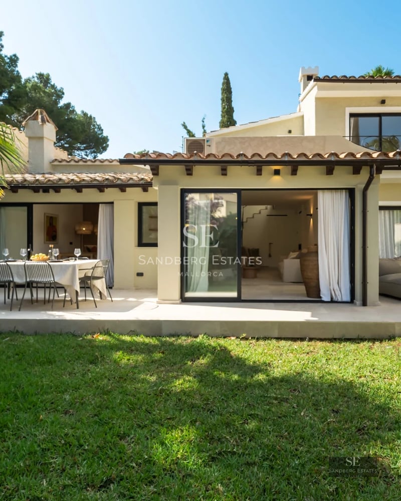 Exterior of a modern villa featuring a reflecting pool, expansive glass windows, and minimalist landscaping. Soft ambient lighting.