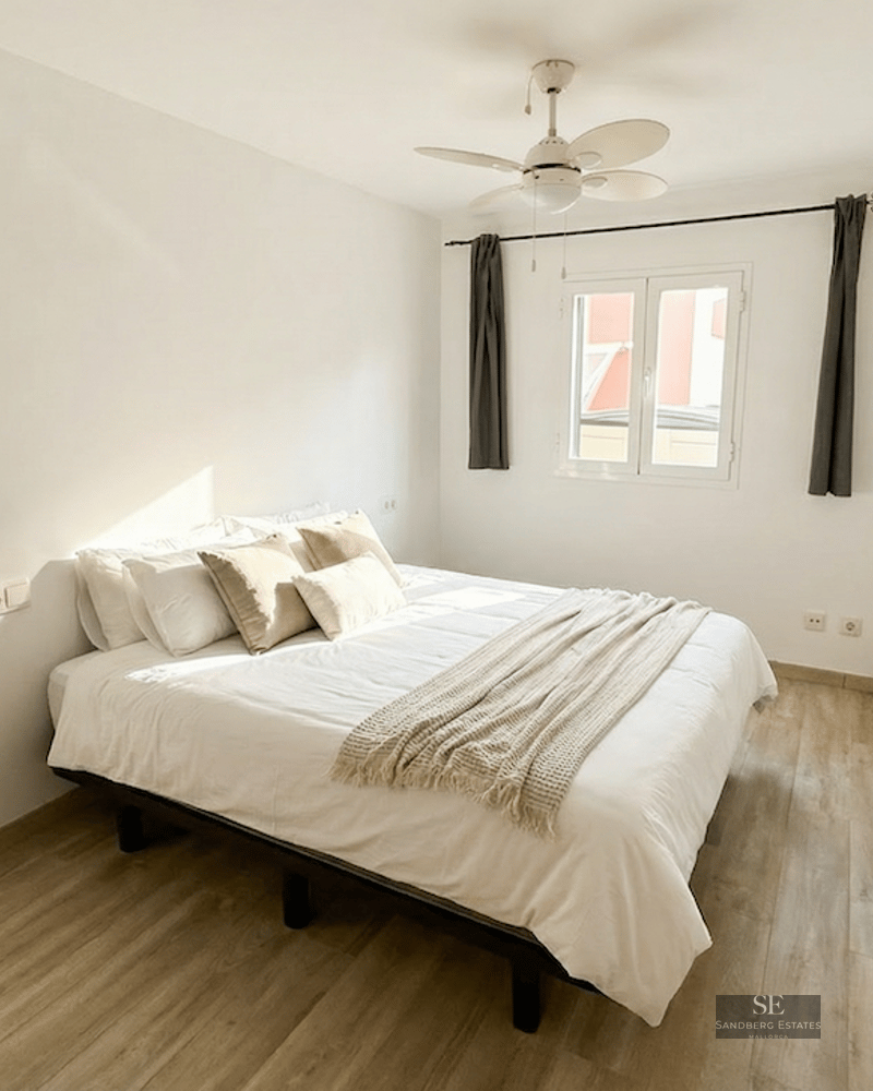 Bright bedroom featuring a white bed, light wood flooring, a white ceiling fan, and natural light.