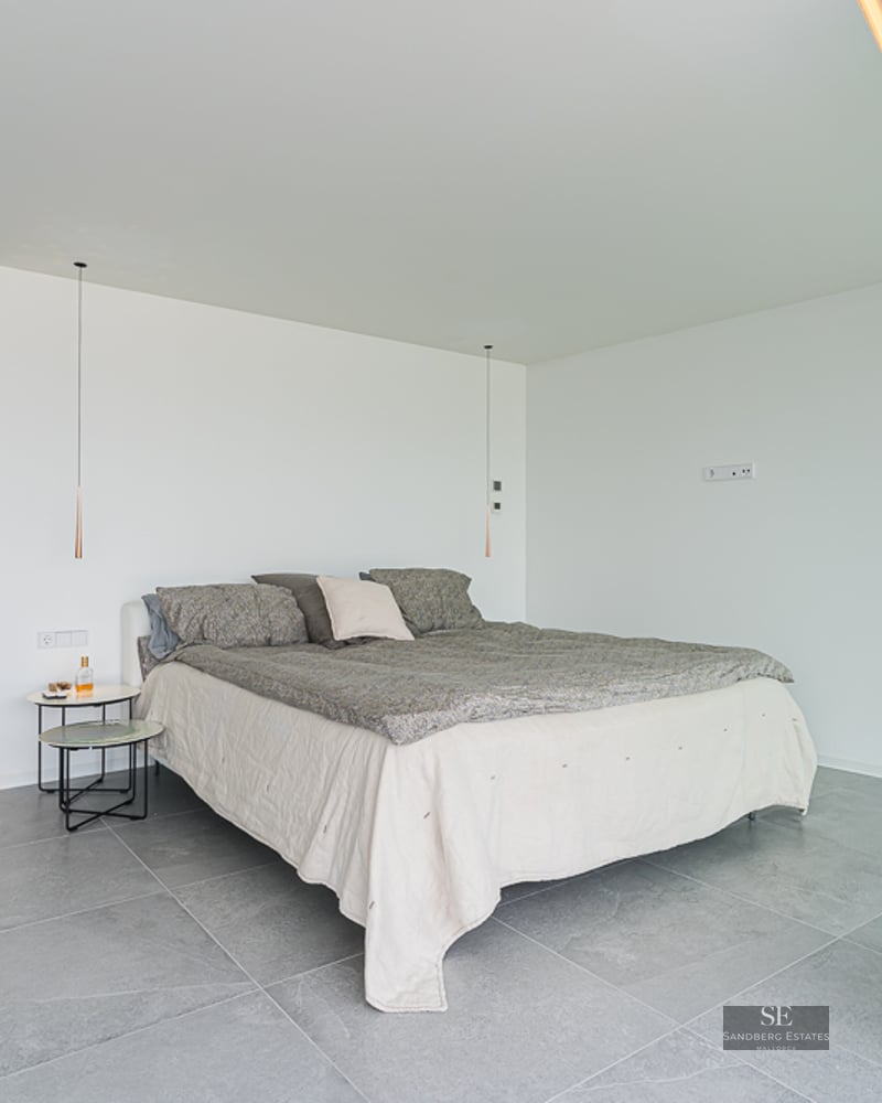 Minimalist bedroom with grey stone floors, white walls, and a large sliding glass door opening to a garden.