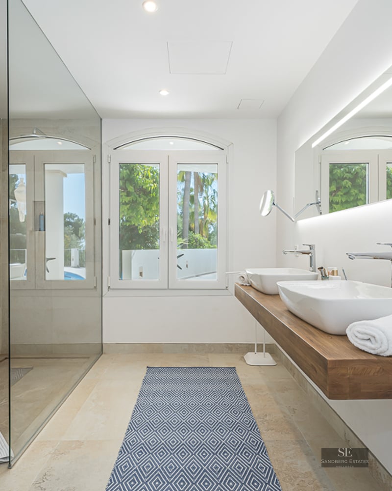Salle de bain moderne avec une grande douche vitrée, double vasque sur plan en bois et vue sur le jardin.