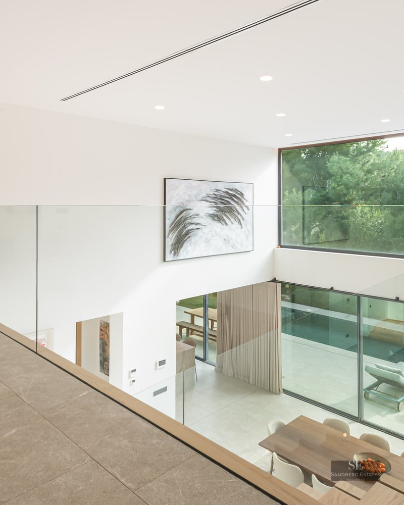 Vue depuis une mezzanine en verre sur un salon à double hauteur avec de grandes baies vitrées donnant sur la piscine.