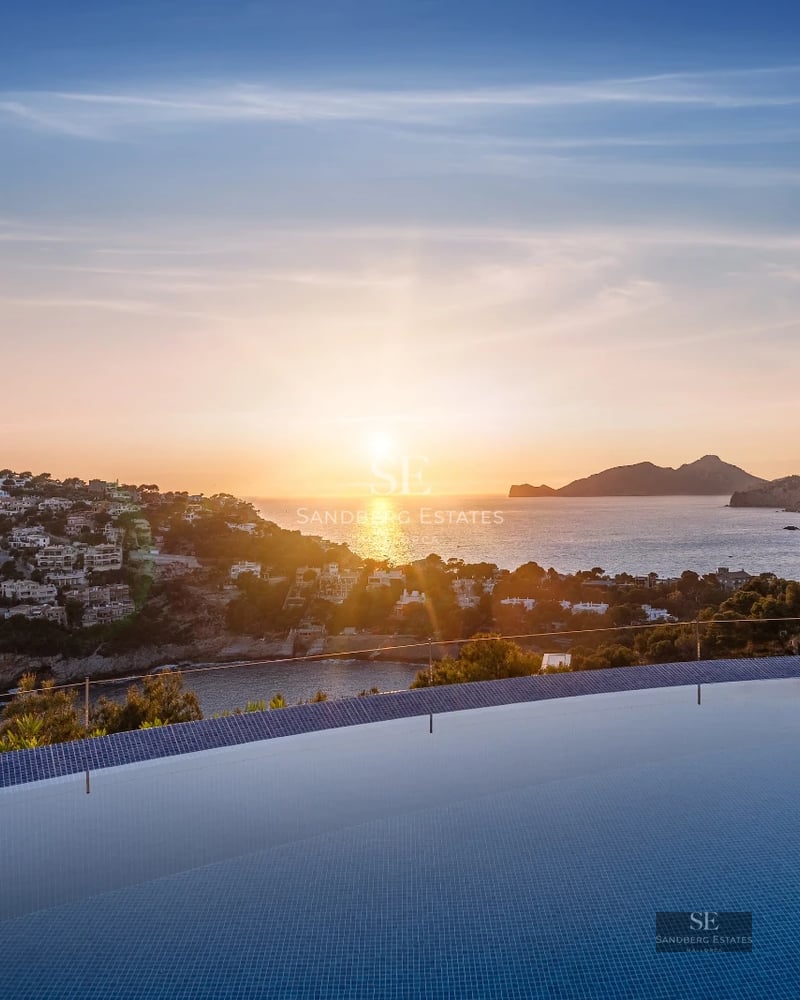 Modern terrace with infinity pool, sea views, designer furniture, and wooden flooring. Glass railing and lush vegetation.