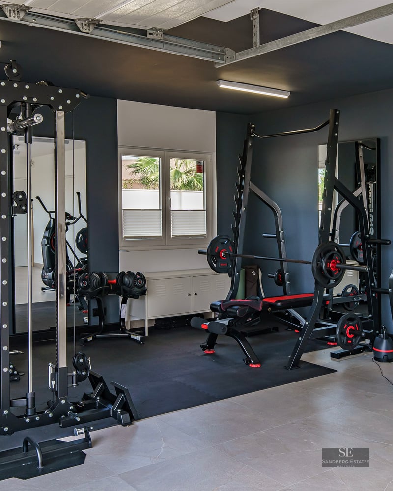 Professional home gym with black weight machines, squat rack, cardio equipment, and large mirrors against dark grey walls.
