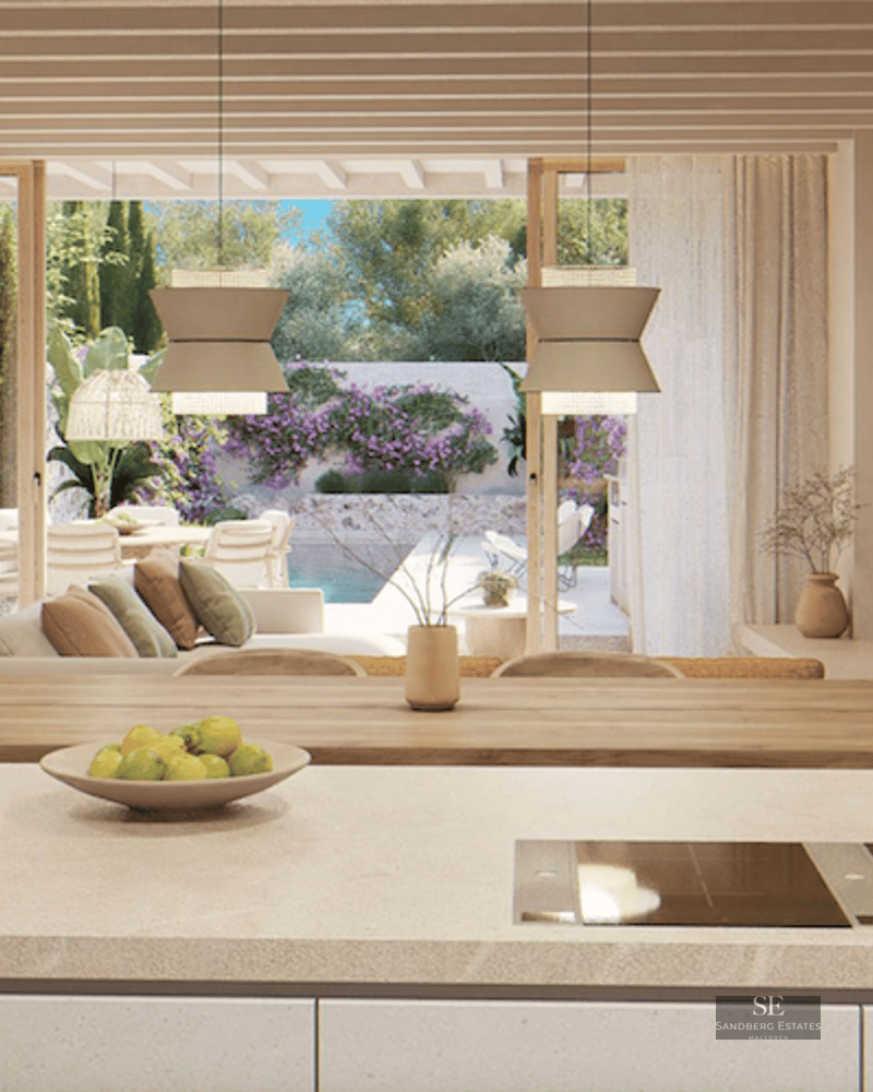 Open-plan space with a kitchen island, wooden beams, and views of a terrace with a pool and garden.