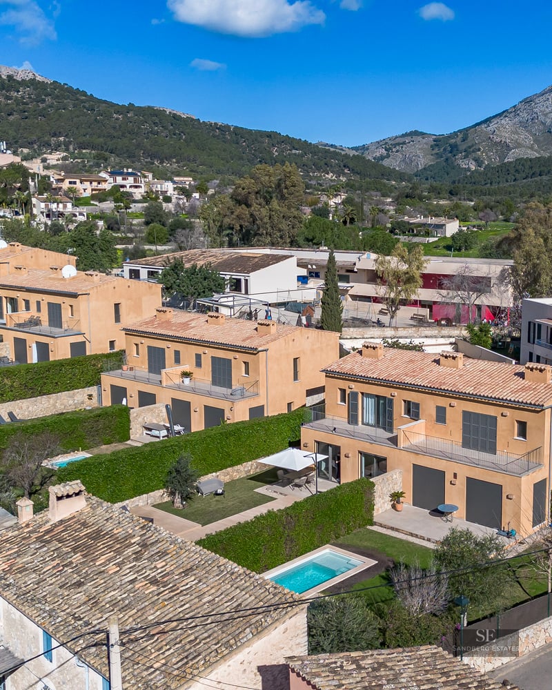 Aerial view of terracotta-colored villas with private pools and green hedges against a mountain backdrop.