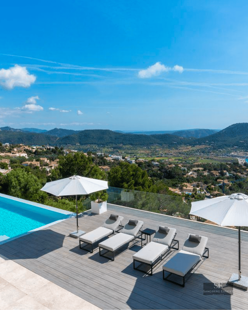 Outdoor terrace featuring a blue swimming pool, modern loungers, white umbrellas, and panoramic mountain and sea views.