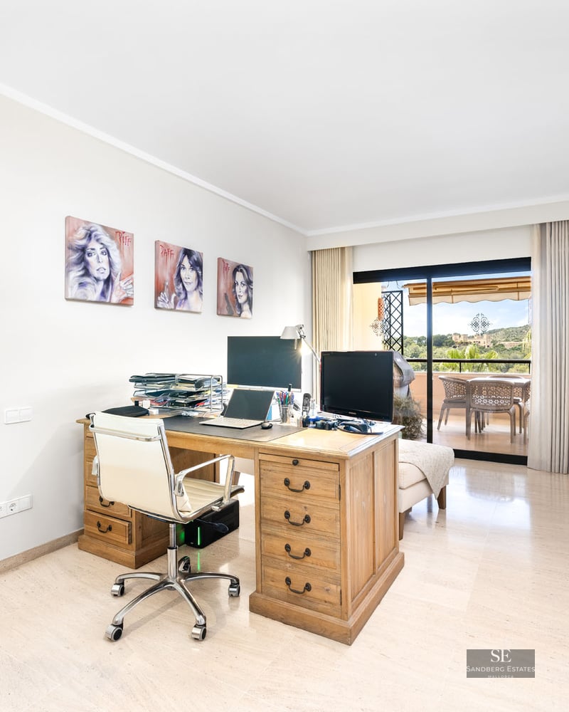 Bureau lumineux avec grand bureau en bois, chaise blanche et baies vitrées ouvrant sur une terrasse.