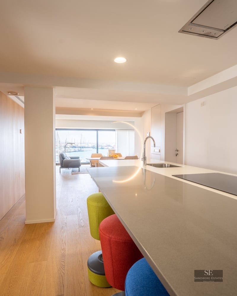 Kitchen island with colorful stools looking through a living area to a marina view through large windows.