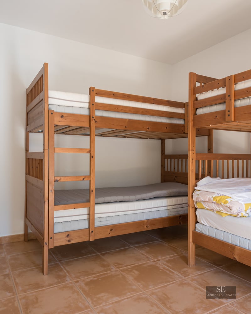 A bright bedroom with two wooden bunk beds and terracotta tiled floors.