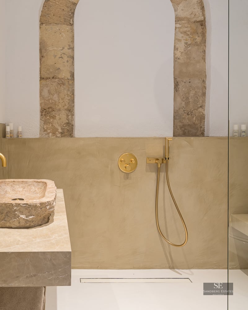 Salle de bain moderne avec vasque en pierre brute, robinetterie dorée et douche à l'italienne avec arche en pierre.