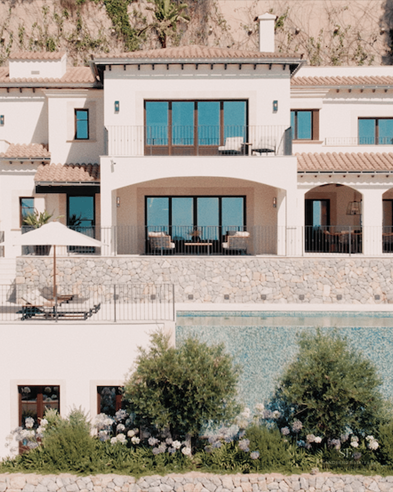 Exterior view of a multi-level white Mediterranean villa featuring a large infinity pool and stone accents.