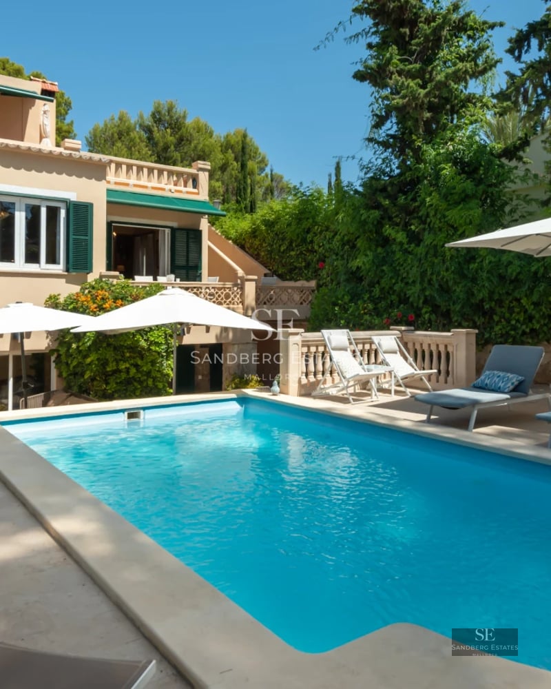 Expansive pool surrounded by lush garden, sun loungers, and a modern house with large windows inviting relaxation.