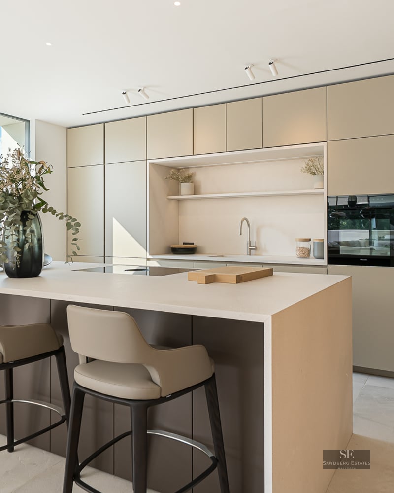 Modern minimalist kitchen featuring a large central island, designer bar stools, and sleek earth-toned cabinetry.