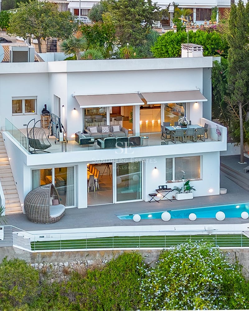 Exterior view of a modern villa featuring a pool, manicured garden, and spacious terraces. Sleek architectural design with warm lighting.