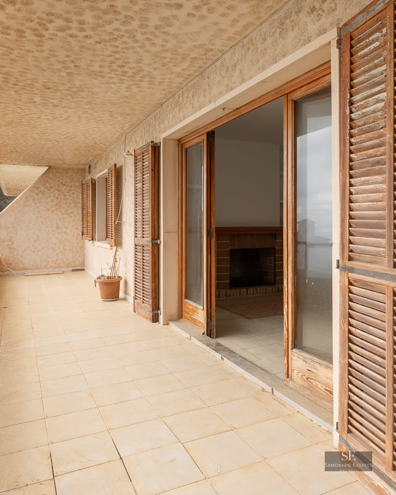 Long tiled balcony with weathered wooden shutters and glass doors leading to an indoor living area.