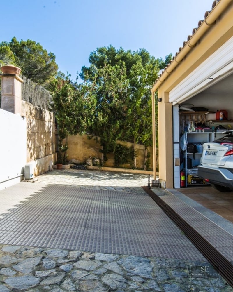 Car parked in a spacious garage next to a natural stone driveway with a large white sliding gate.