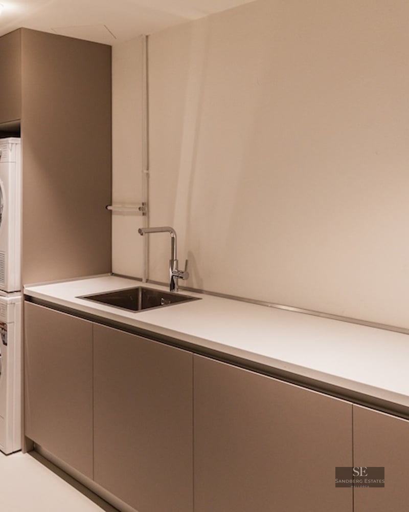 Modern laundry room with stacked washer and dryer, long white countertop, and integrated stainless steel sink.