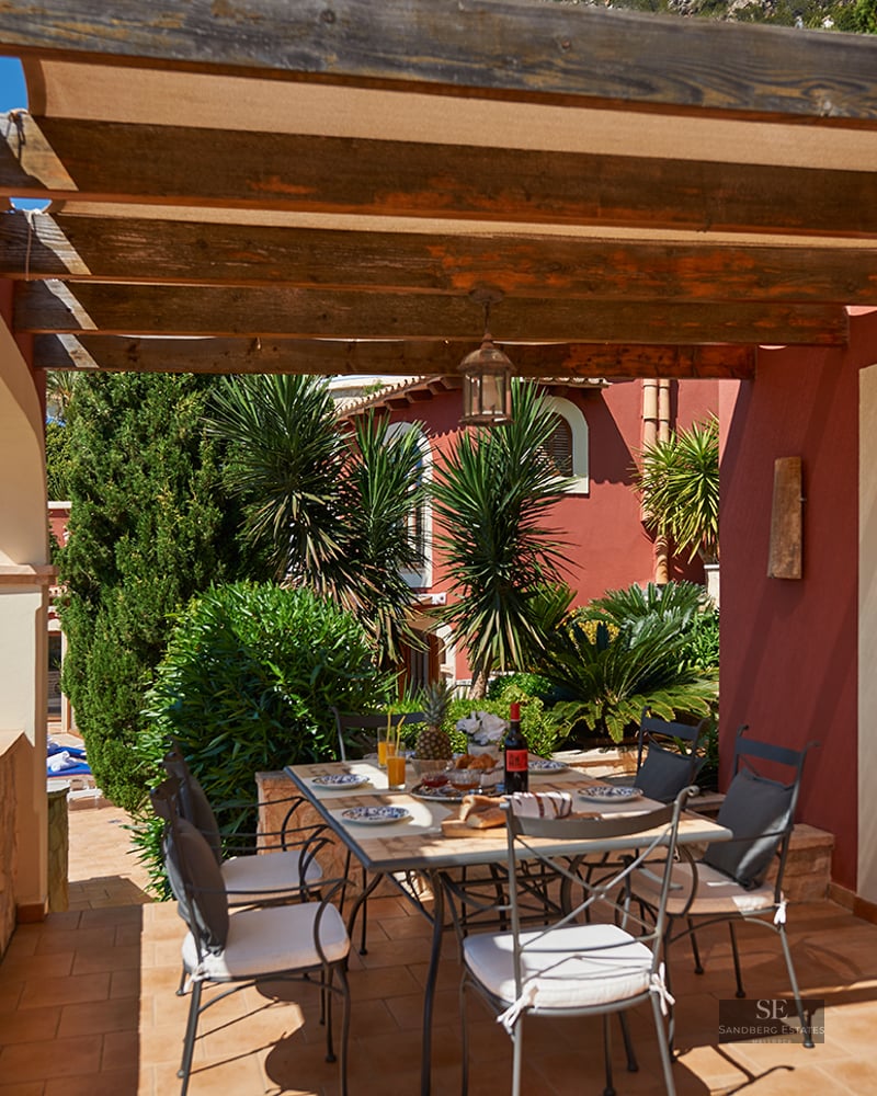 Covered terrace with a wooden pergola and dining table overlooking a tropical garden.