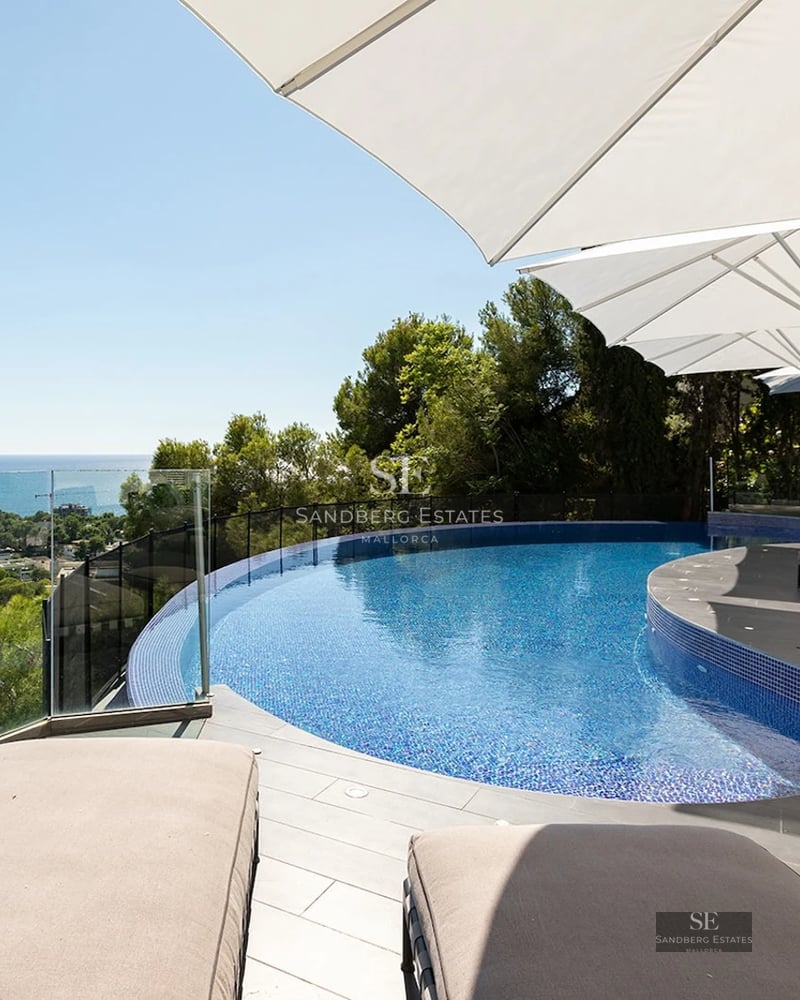 Curved infinity pool on a modern terrace with white umbrellas and loungers overlooking the Mediterranean sea.