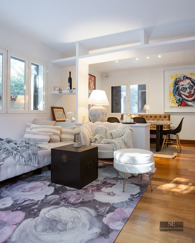 Open-plan living room with white sofas, floral rug, wood floors, and a dining area in the background.