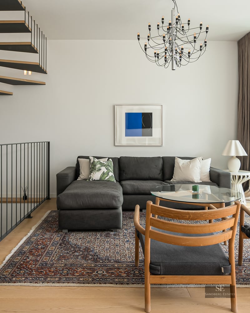 Contemporary living room featuring a gray sectional, wooden spiral stairs, and floor-to-ceiling windows.