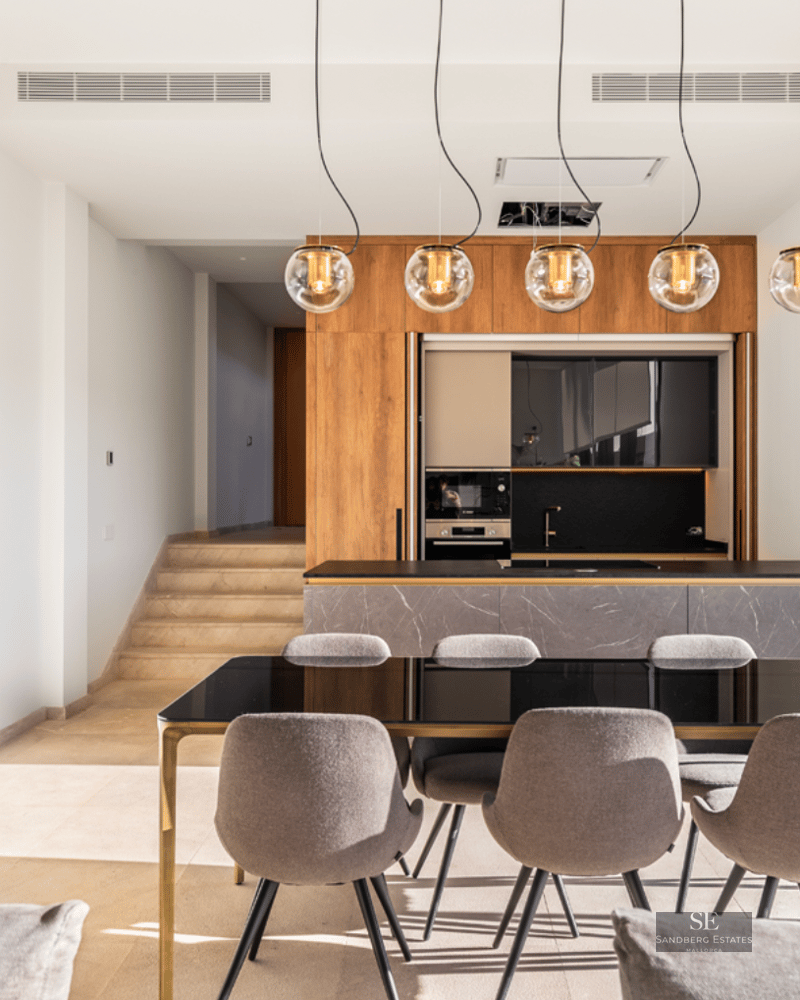 Modern dining room featuring a black glass table, grey chairs, designer pendant lights, and a marble kitchen island.
