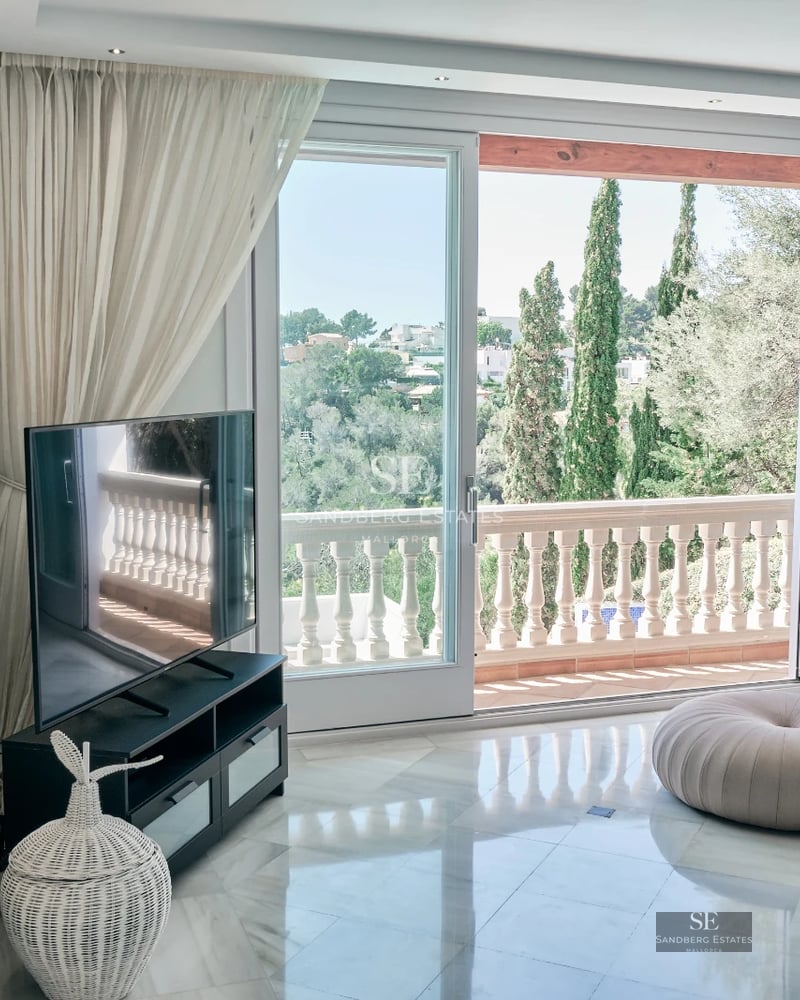 View of infinity pool with modern design and sun loungers. Well-maintained garden with lush vegetation. Clear blue sky in the background.