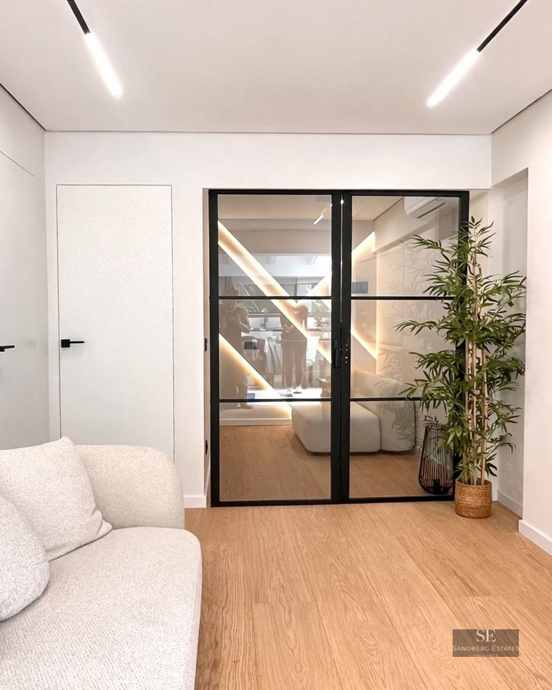 Modern living room featuring a white textured sofa, light wood floors, and black-framed glass double doors.