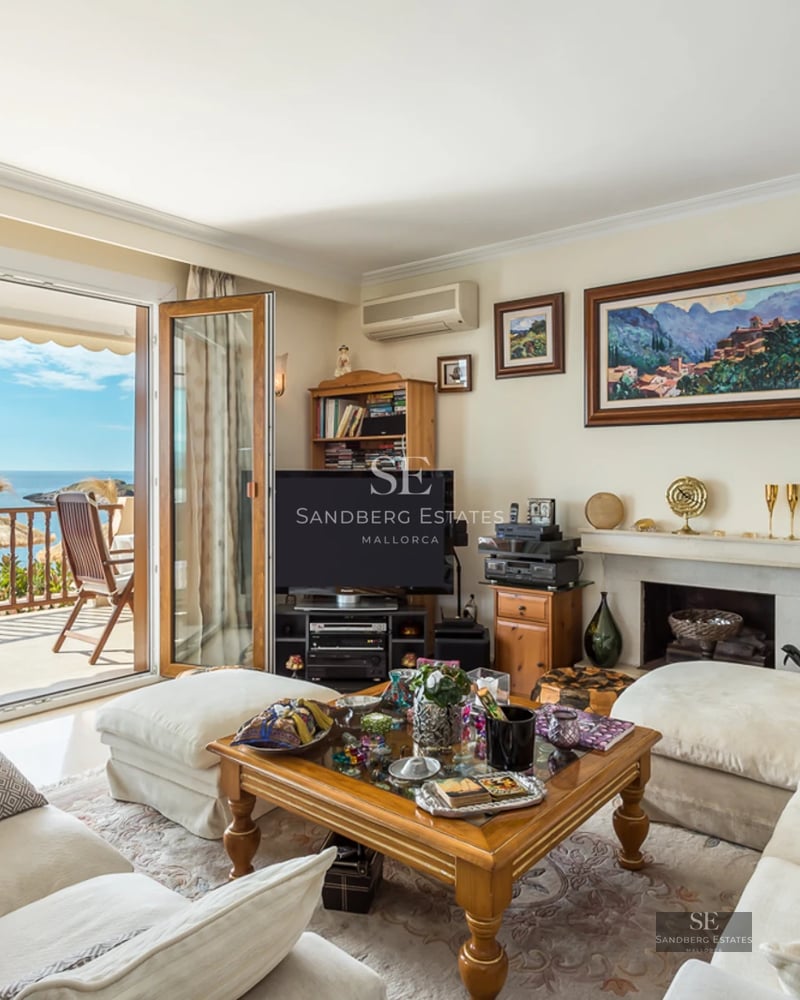 Bright living room with white sofas and a wooden coffee table opening to a terrace with Mediterranean sea views.