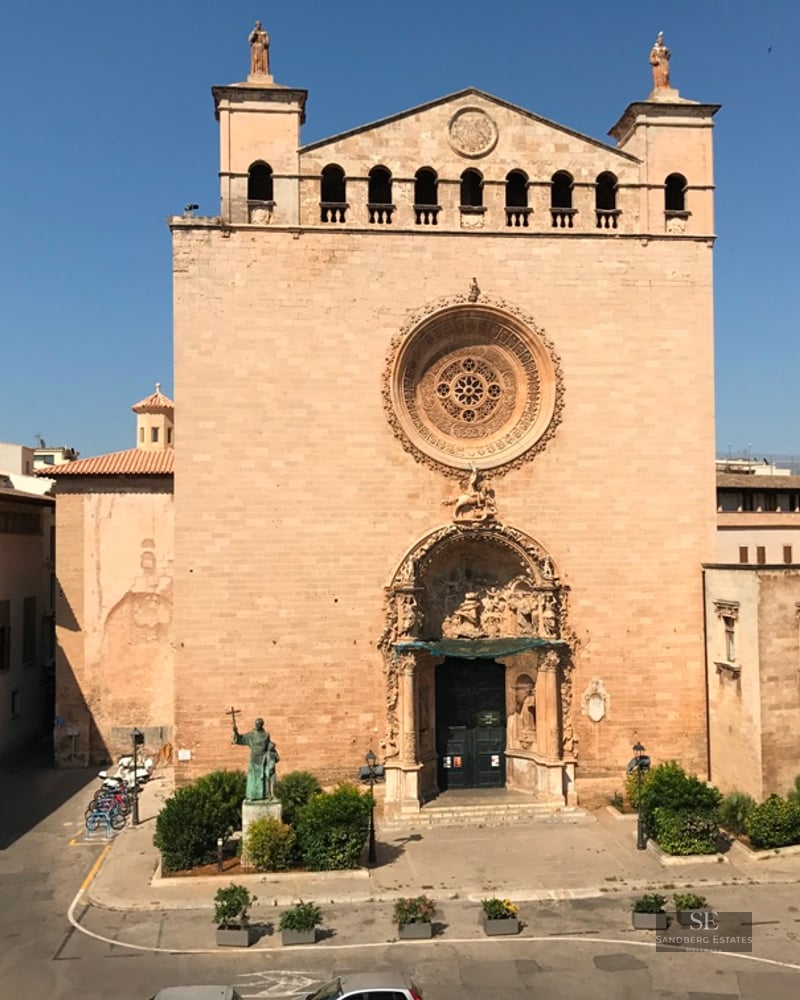 Facade of a historic stone church with a large ornate rose window and a decorative arched entrance on a sunny day.
