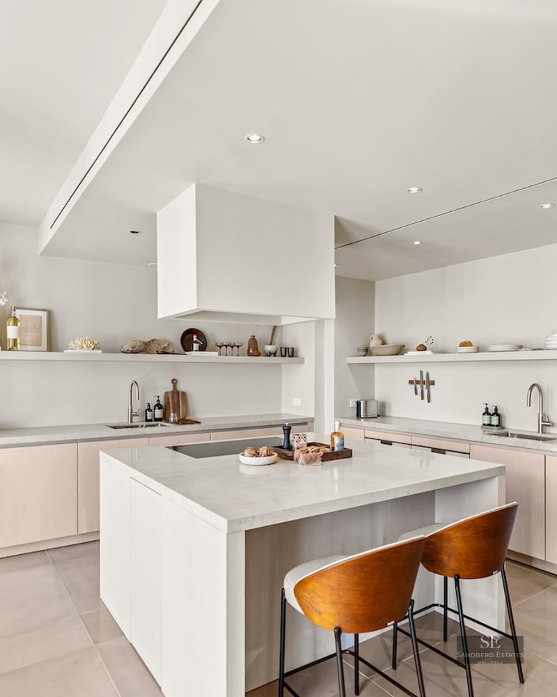 Bright modern kitchen with white island, stone countertops, wine cooler, and warm wood bar stools.