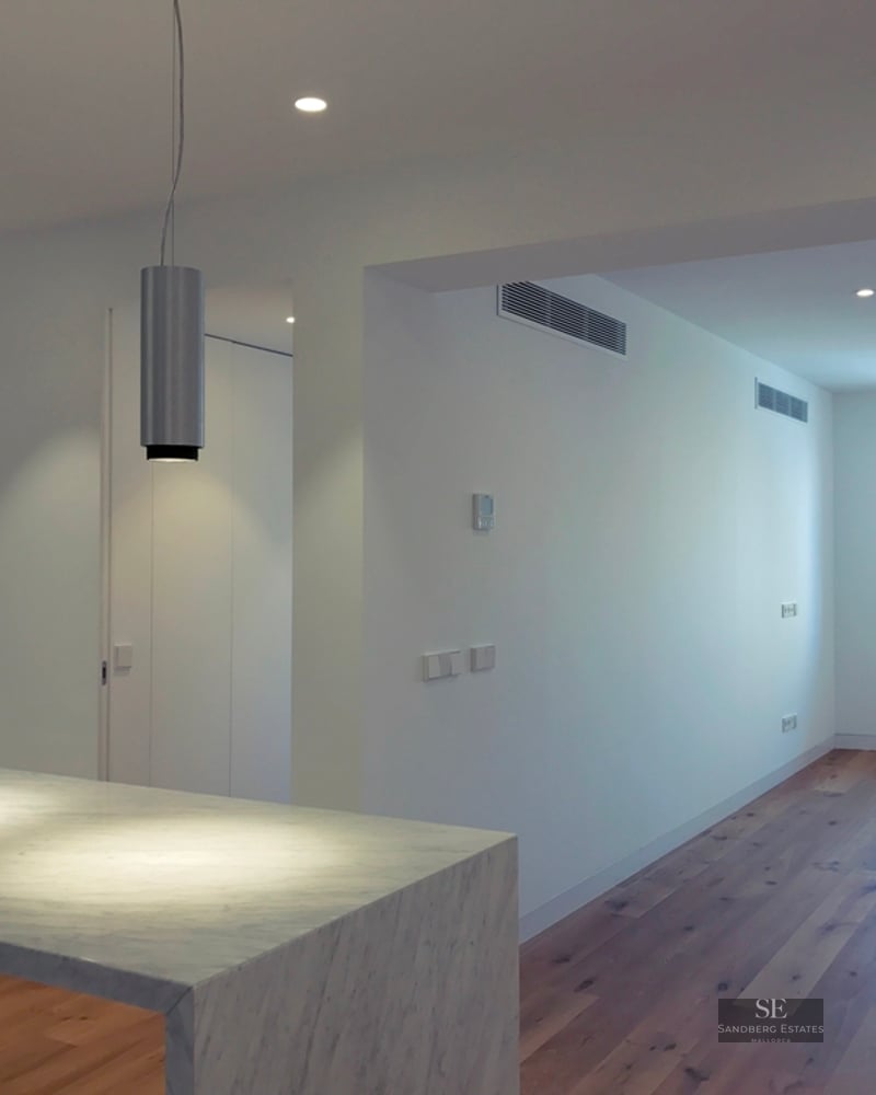 Modern kitchen featuring a white marble island and wood flooring leading into a bright living area.