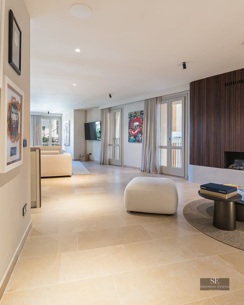 Modern living room featuring a wood-slat fireplace wall, stone floors, and framed music memorabilia in a hallway.