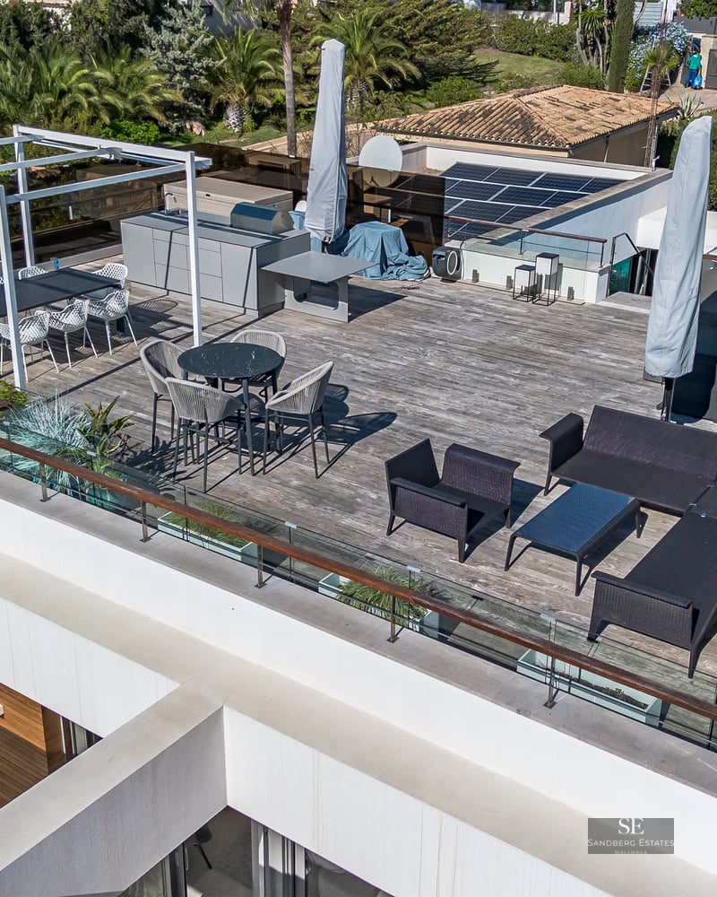 Vue aérienne d'une terrasse de toit moderne avec salon, espace repas, cuisine extérieure et garde-corps en verre.