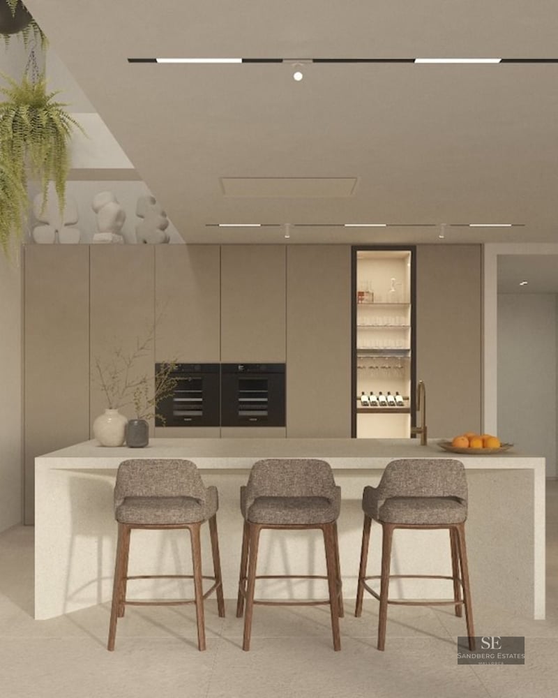 Modern kitchen with stone island, bar stools, hanging ferns, and integrated appliances against beige walls.